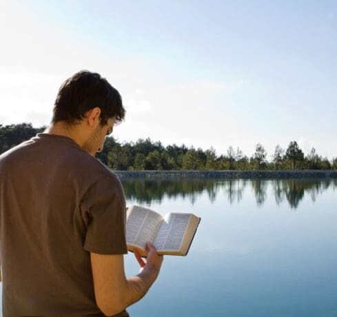 Young man in front of lake reading the Bible